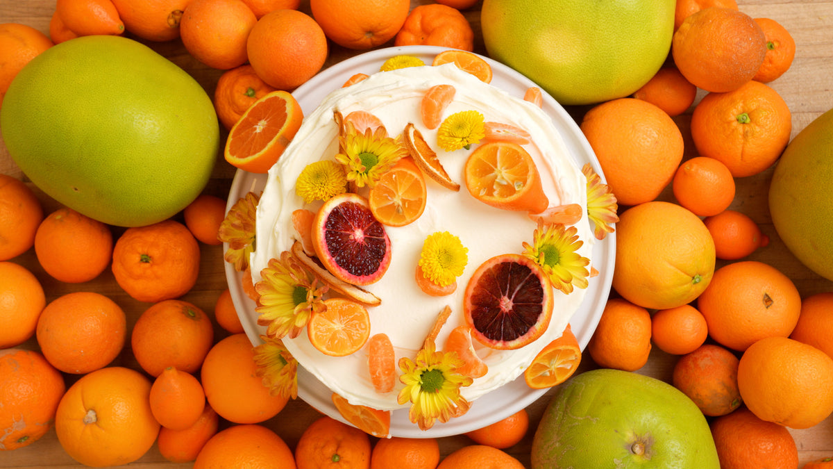 Cake with orange slices and flowers surrounded by oranges and limes on a wooden surface