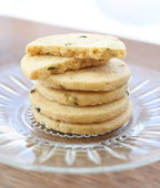 A stack of Valerie Confections’ Rosemary & Polenta Cookies on a glass plate, showcasing their golden crisp texture and flecks of fresh rosemary.